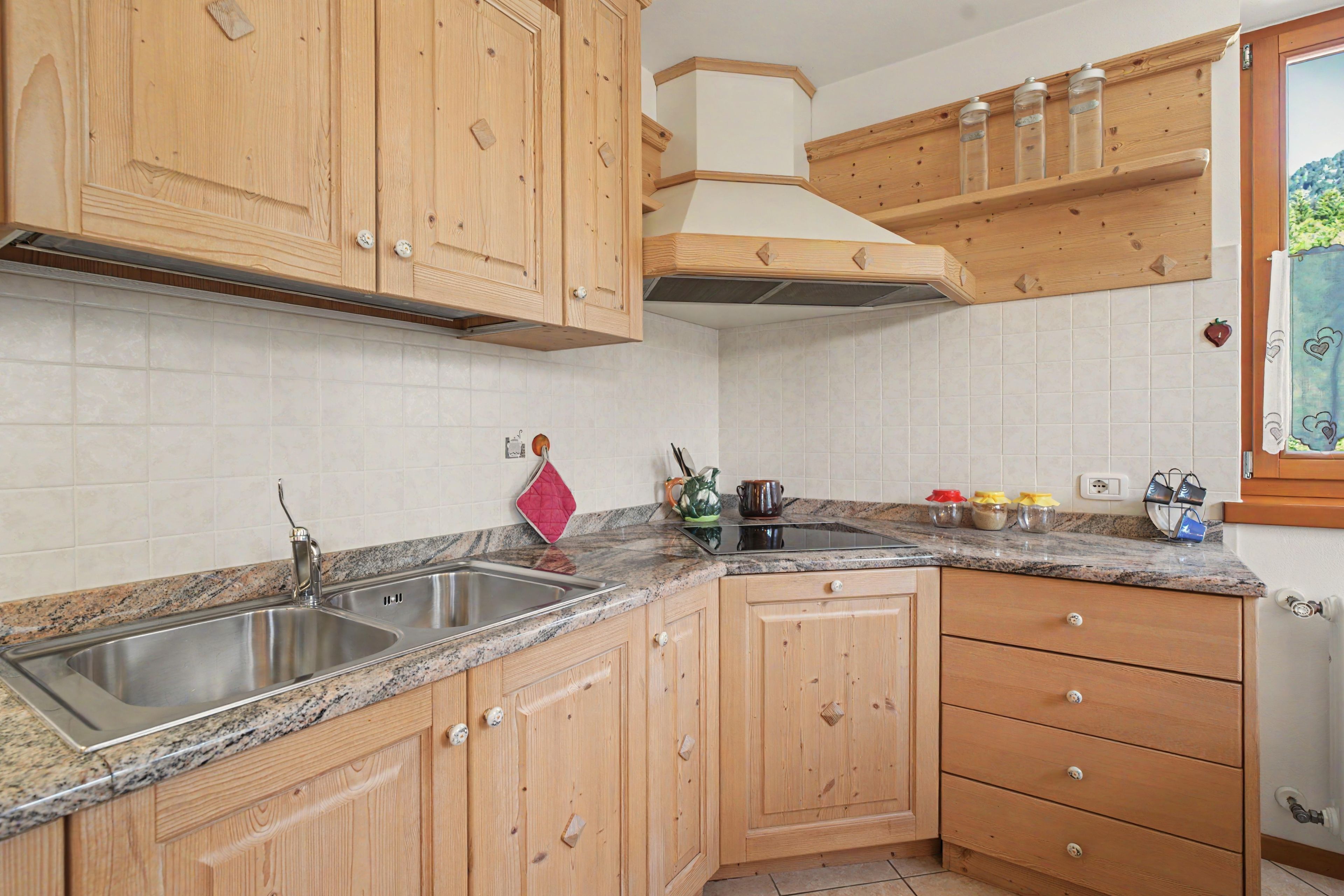 A kitchen with wooden cabinets, a granite countertop, a stainless steel sink, and a window with a view of greenery.
