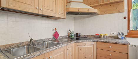 A kitchen with wooden cabinets, a granite countertop, a stainless steel sink, and a window with a view of greenery.