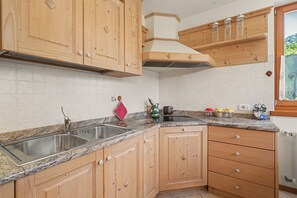 A kitchen with wooden cabinets, a granite countertop, a stainless steel sink, and a window with a view of greenery.