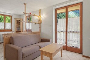 Un salón con sofá, una mesa de madera, un espejo y una puerta que da a zonas verdes.