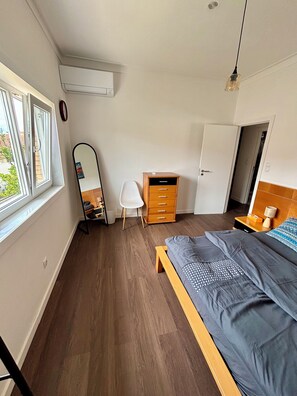 Ein Schlafzimmer mit Bett, Schreibtisch, Stuhl, Kleiderschrank, Spiegel und Fenster.