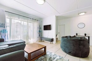 Ett modernt vardagsrum med en soffa, ett soffbord, en sittpuff och en platt-TV som är monterad på väggen.