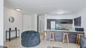Ett modernt kök med en central köksö, trästolar och en sittpuff i ett vardagsrum.