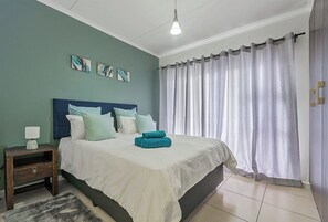 Ein Schlafzimmer mit Bett, Nachttisch und Blick ins Freie durch Vorhänge.
