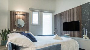 Ett modernt hotellrum med en säng, en tv, en spegel och en krukväxt.