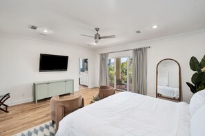 Una camera da letto moderna con un letto, una televisione, una ventola a soffitto, una porta scorrevole su un balcone e un grande specchio.
