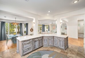 A modern kitchen with a large island, wooden cabinets, and a dining area with a table and chairs. - Designer family retreat with a private pool, spa, three outdoor decks, and resort amenities—all just minutes from Destin's beautiful white sand beaches. (Destin)