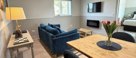A modern, well-lit room with a sofa, a dining table, a TV, and a window with a view.