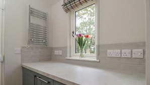 Una cocina con ventana, un perchero y un florero con flores.
