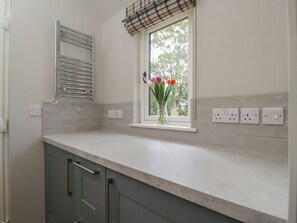 Eine Küche mit Fenster, Handtuchhalter und Blumen in einer Vase.