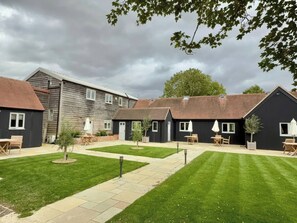A courtyard with a lawn, outdoor seating, and a building with a dark facade. - Foxglove (Bicester)