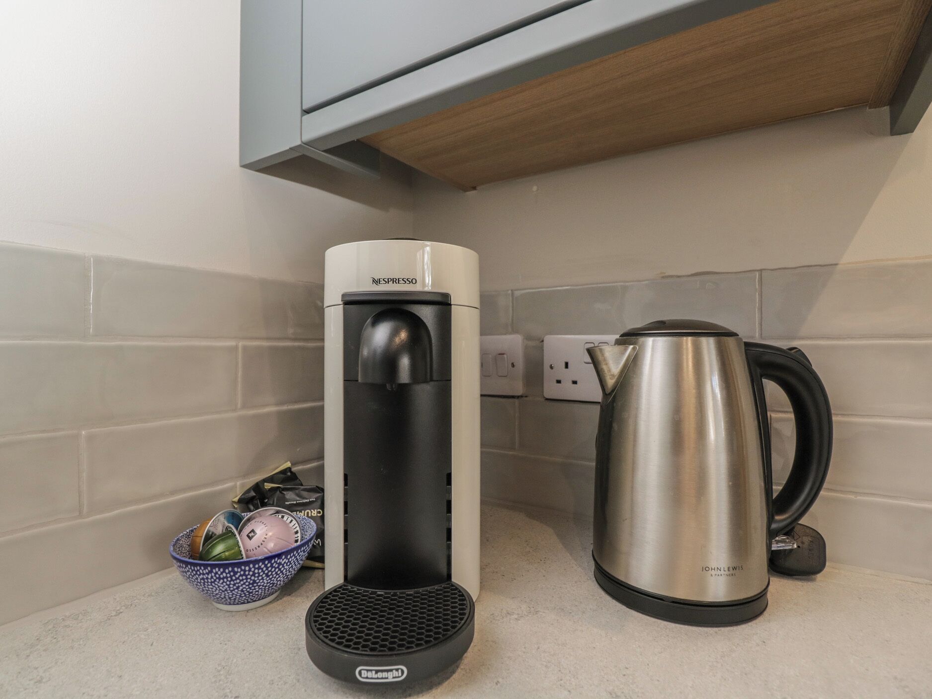 Ett kök med en kaffemaskin, en vattenkokare och en korg med frukt.