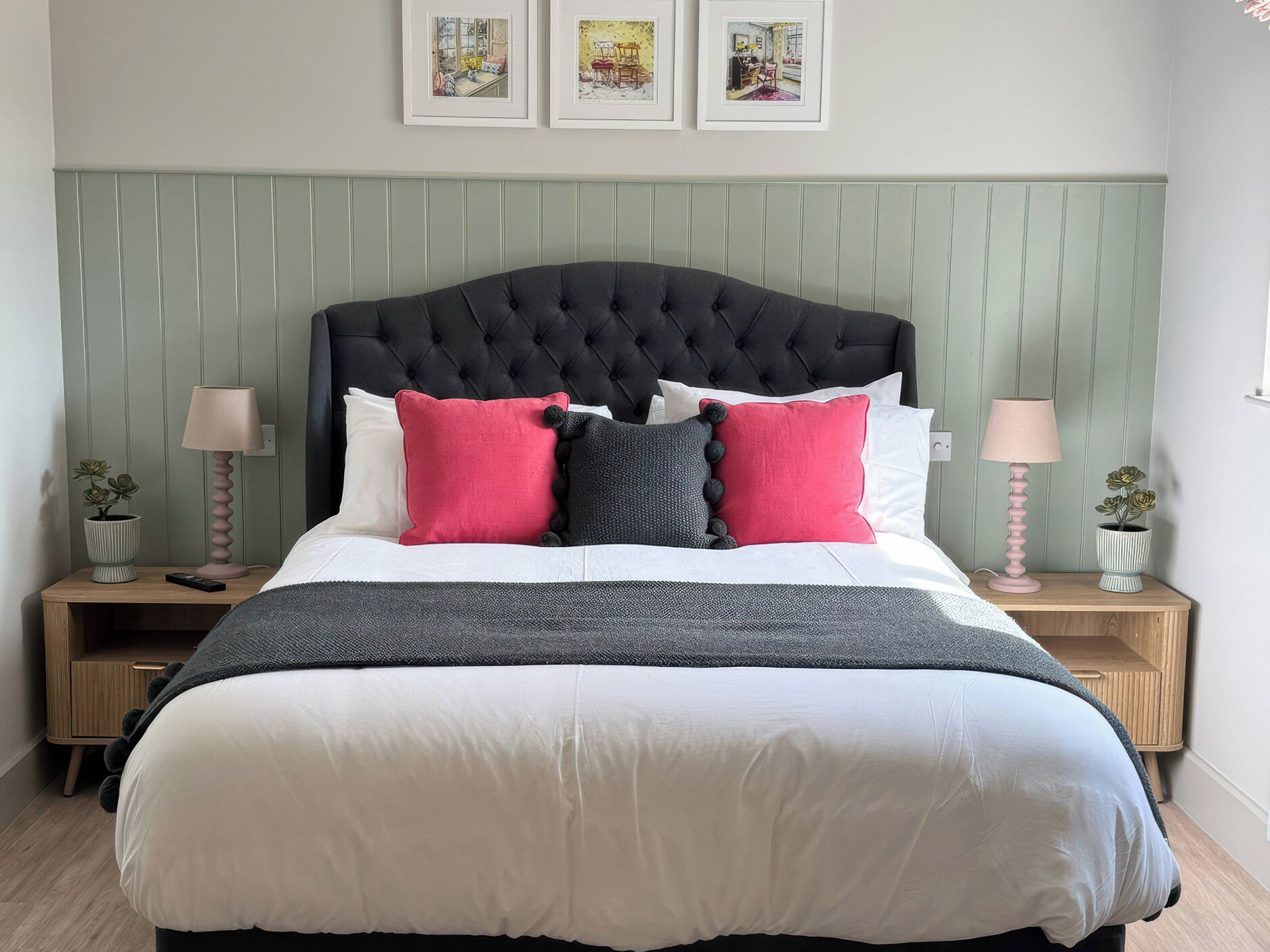 A neatly made bed with a tufted headboard, two bedside tables with lamps, and three framed pictures on the wall.