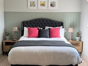 A neatly made bed with a tufted headboard, two bedside tables with lamps, and three framed pictures on the wall.