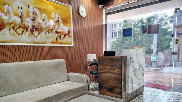 Et receptionområde med sofa, sofabord med glasplade, træreceptionistskrivebord og væguret.