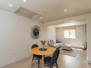 A modern living room with a round dining table, a sofa, and a window with a patterned valance. - Poppy Patch (Bicester)