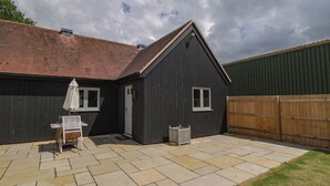 A dark wooden building with a tiled patio, a white door, and a window. - Poppy Patch (Bicester)