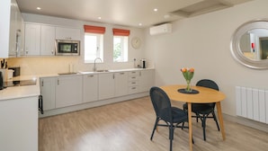 A modern kitchen with white cabinets, a microwave, a sink, and a dining area with a table and chairs. - Poppy Patch (Bicester)