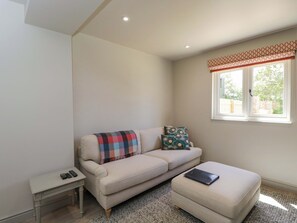 Ein Wohnzimmer mit einer Couch, einem kleinen Tisch, einem Fenster mit einem gemusterten Vorhang und Blick auf Grünflächen.
