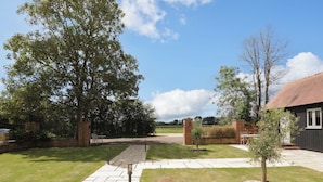 A paved pathway leading to a building with a brick wall and a small tree in the center. - Poppy Patch (Bicester)