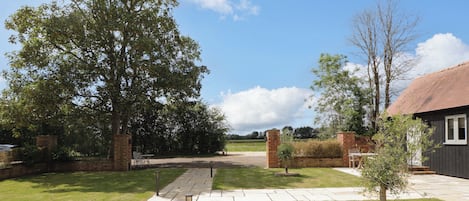 A paved pathway leading to a building with a brick wall and a small tree in the center.