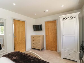 Ein Schlafzimmer mit zwei Holztüren, einem über einer Kommode befestigten Fernseher und einem großen, weißen Schrank.