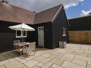 Ein schwarzes Gebäude mit einer gefliesten Terrasse, einer weißen Tür und einem Fenster.