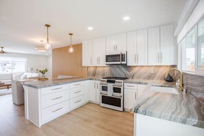 A modern kitchen with white cabinetry, a central island with a built-in stove, and pendant lighting. - Charming Encinitas Retreat Near Local Beaches (Encinitas)