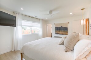 A bedroom with a bed, a ceiling fan, a TV, and a window with curtains. - Charming Encinitas Retreat Near Local Beaches (Encinitas)
