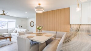 A modern living room with a white sofa, a dining table with placemats, and a kitchen area with a marble countertop. - Charming Encinitas Retreat Near Local Beaches (Encinitas)