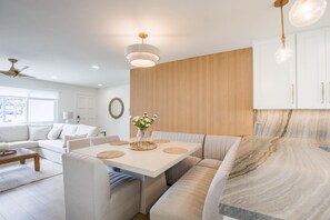 A modern living room with a white sofa, a dining table with placemats, and a kitchen area with a marble countertop. - Charming Encinitas Retreat Near Local Beaches (Encinitas)