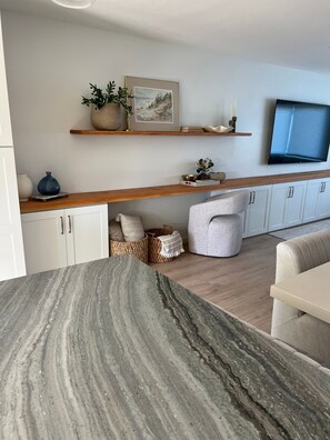 A modern living room with a marble countertop, a sofa, a television, and a wooden shelf with decorative items. - Charming Encinitas Retreat Near Local Beaches (Encinitas)