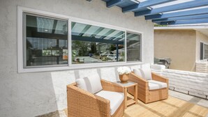 A covered outdoor seating area with wicker furniture and a large window. - Charming Encinitas Retreat Near Local Beaches (Encinitas)