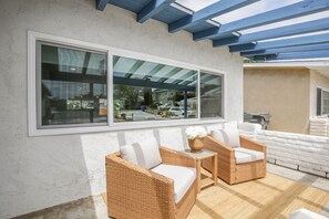 A covered outdoor seating area with wicker furniture and a large window. - Charming Encinitas Retreat Near Local Beaches (Encinitas)