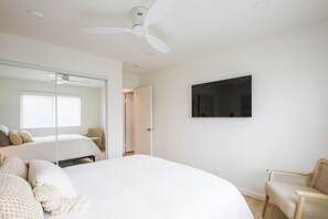 Ein Schlafzimmer mit Bett, Sessel, Fernseher und Deckenventilator.