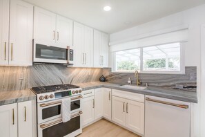 A modern kitchen with white cabinets, a gas stove, a microwave, and a large window providing natural light. - Charming Encinitas Retreat Near Local Beaches (Encinitas)