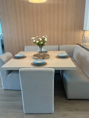 A modern dining area with a square table, four chairs, and a vase of white flowers. - Charming Encinitas Retreat Near Local Beaches (Encinitas)