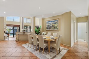A dining area with a table set for six, surrounded by chairs, a painting on the wall, and a view of the outdoors. - Spacious, sun-drenched 5-bedroom home in prime Applecross. Featuring a private pool, indoor pool table, secure outdoor spaces, and high ceilings, this retreat is designed for unforgettable family memories by the river. (Applecross)