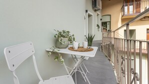 Un balcon avec une chaise blanche, une petite table sur laquelle est posée une plante, une tasse blanche et un pichet blanc.