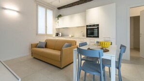 Une cuisine moderne avec des meubles blancs, un four noir et un coin repas comprenant une table blanche et des chaises bleues.