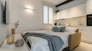 Une chambre moderne avec un lit, une table de chevet et une vue sur la cuisine adjacente.