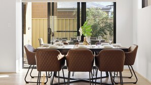 Zona pranzo con tavolo apparecchiato per sei, ampie finestre e vista su una recinzione e alberi.
