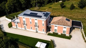 A two-story building with a flat roof and solar panels, surrounded by greenery and a gravel driveway.