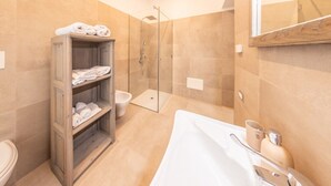 A modern bathroom with a glass shower enclosure, a wooden towel rack, and a bathtub with a white towel.
