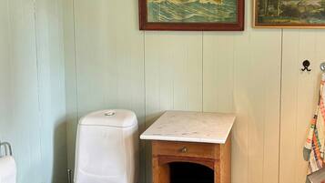 A bathroom with a toilet, a wooden cabinet, a trash can, and two framed pictures on the wall.