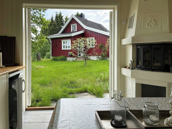 A kitchen with a view of a red house, a window, and a small garden.