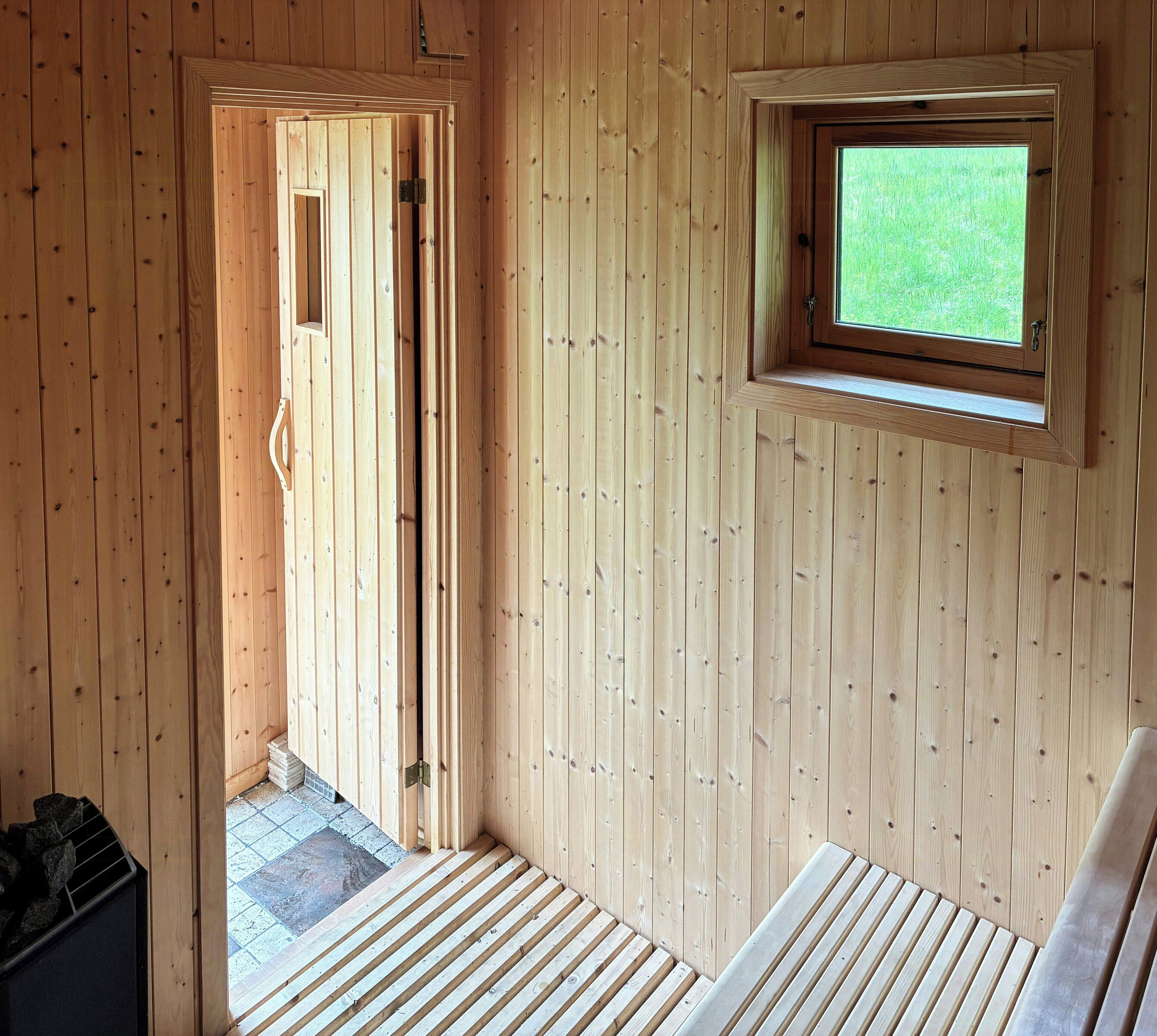 A wooden room with a door leading outside, a window, and a bench.