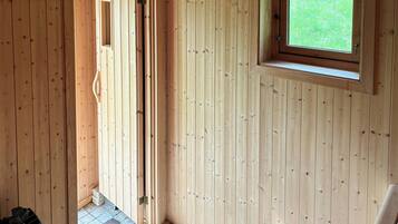 A wooden room with a door leading outside, a window, and a bench.