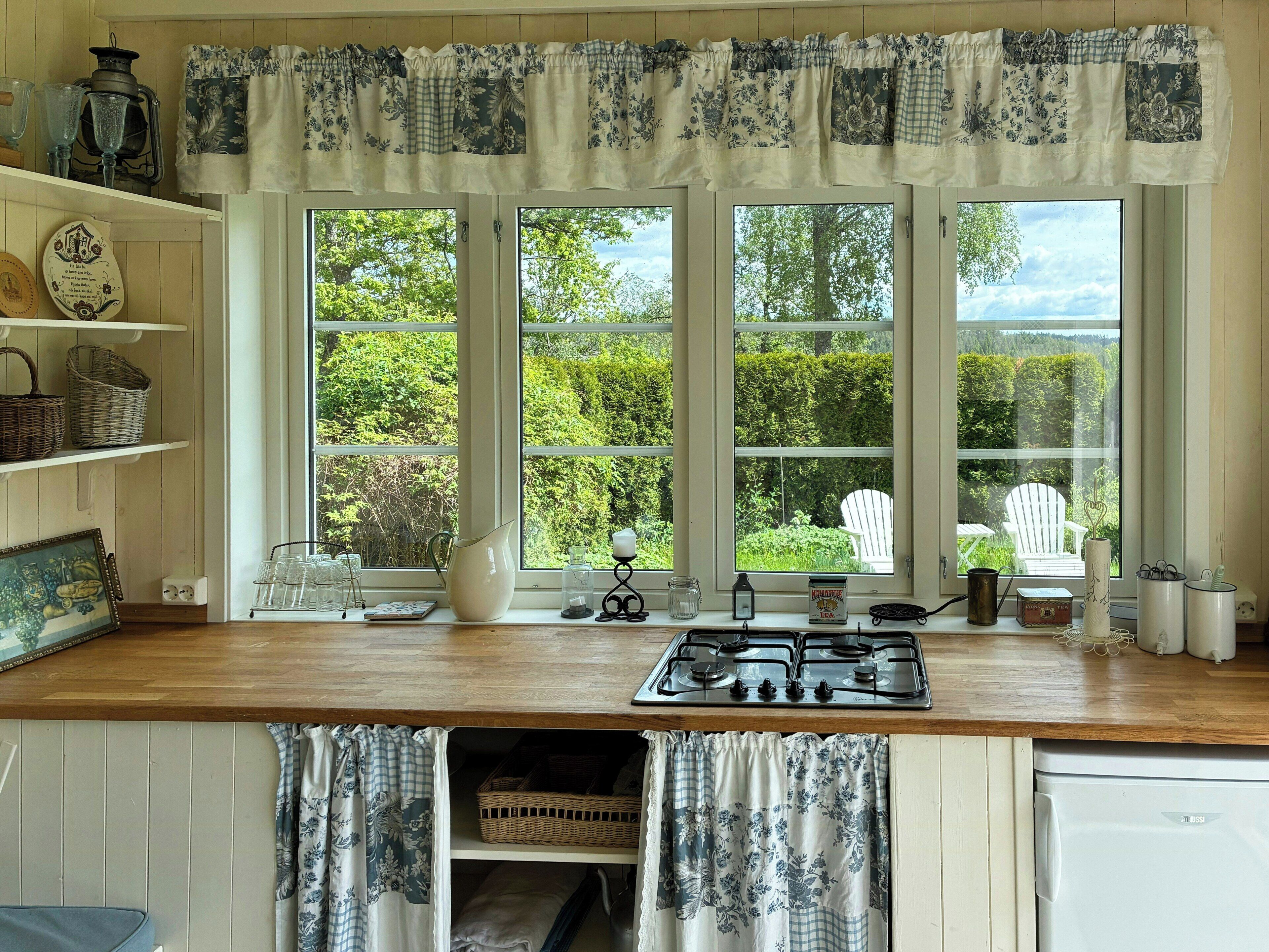 A kitchen with a stove, large windows, and a view of greenery outside.