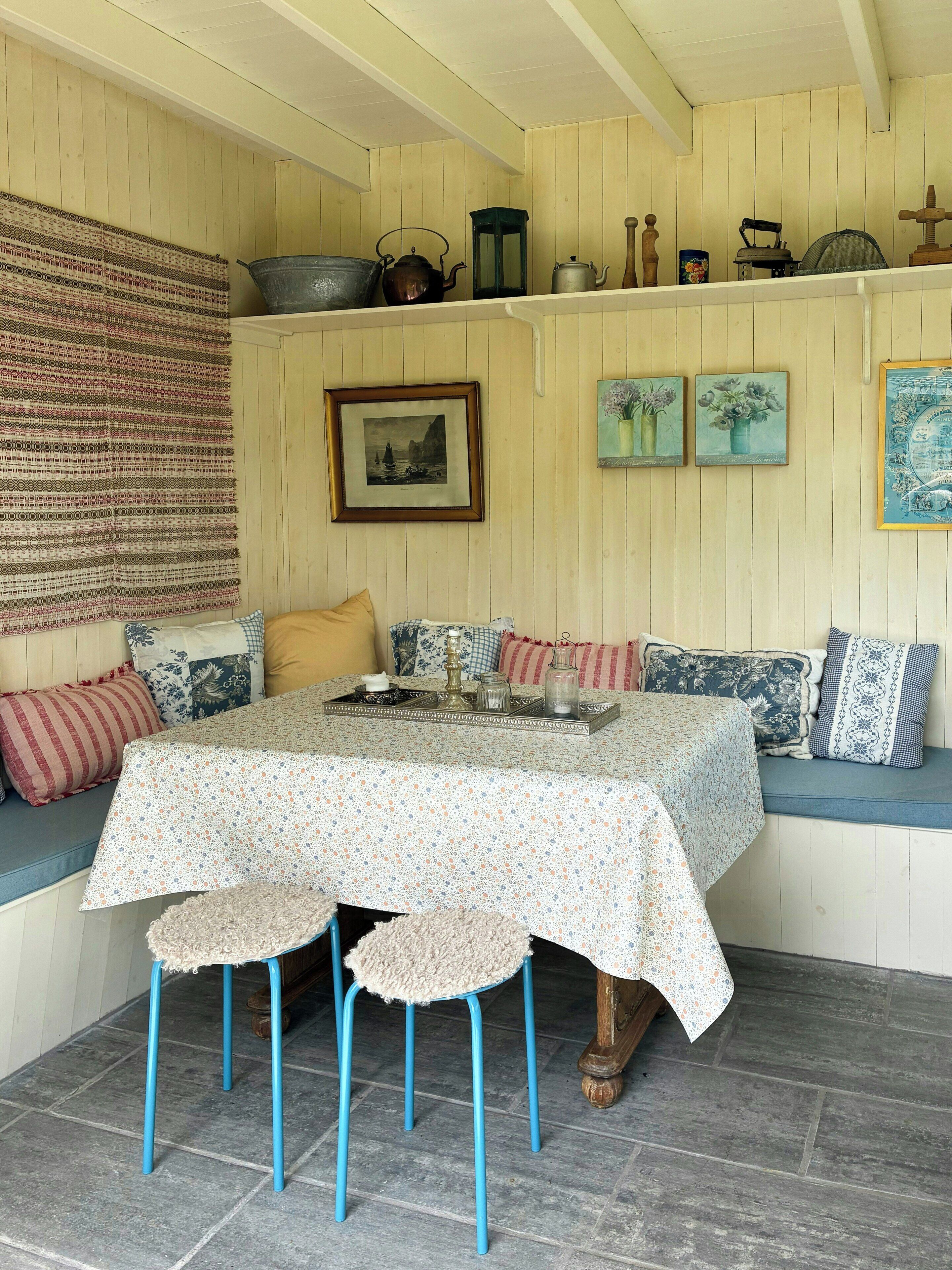 A cozy room with a wooden bench, a table with a floral tablecloth, and various decorative items on the wall.